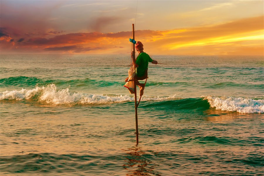 A fisherman sits on a pole out at sea at sunset in Sri Lanka