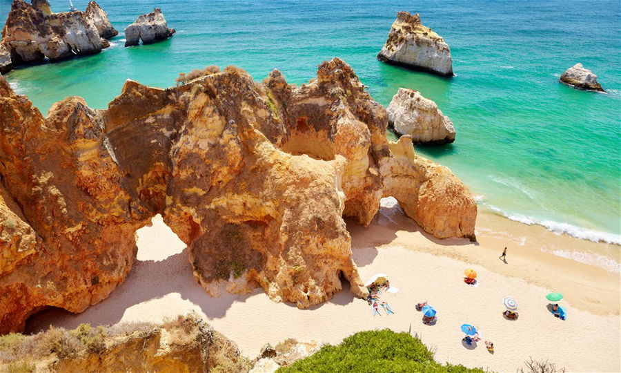 A golden sand beach in Portugal surrounded by rugged rocks with the clear blue ocean in the background