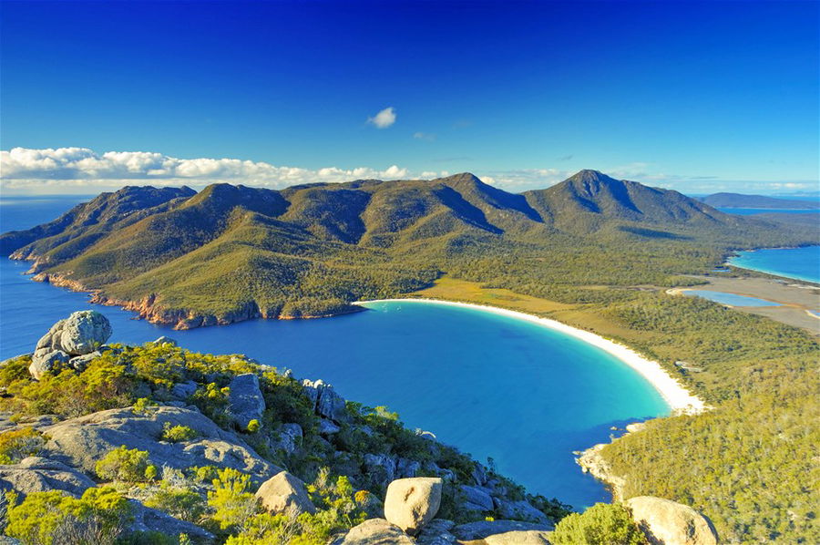 An aerial view of a white sand beach with green mountains as the backdrop in Tasmania