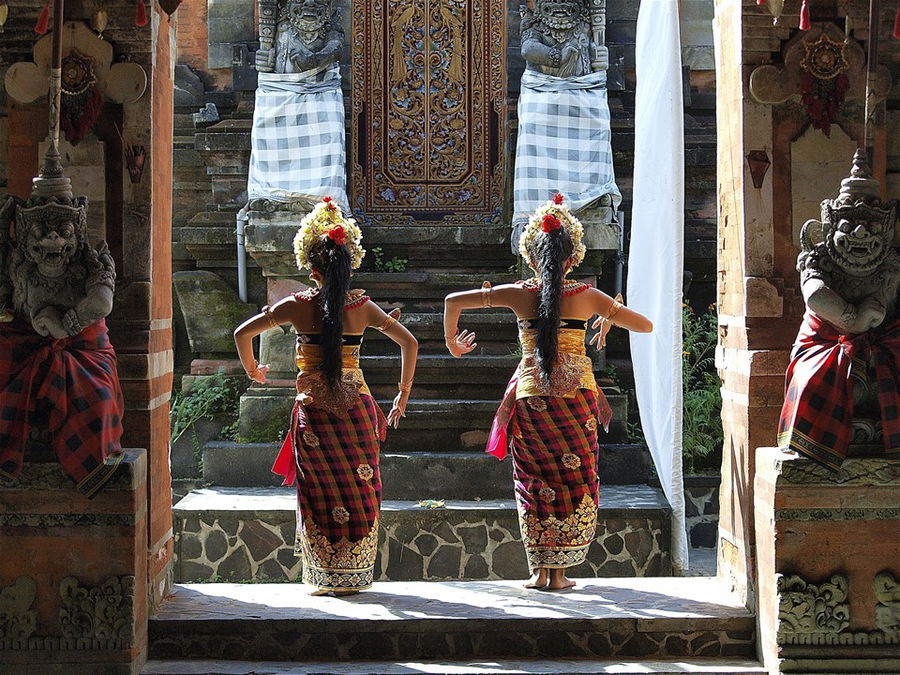 Two young girls in traditional dress perform a dance in front of an ornate temple, Bali