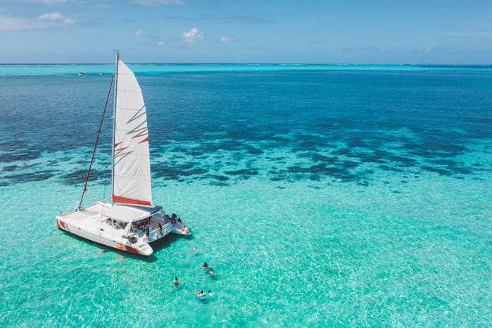 Family And Friends Swimming Near A Beautiful Catamaran In The Paradise Turquoise Lagoon Of The East Coast Of Mauritius