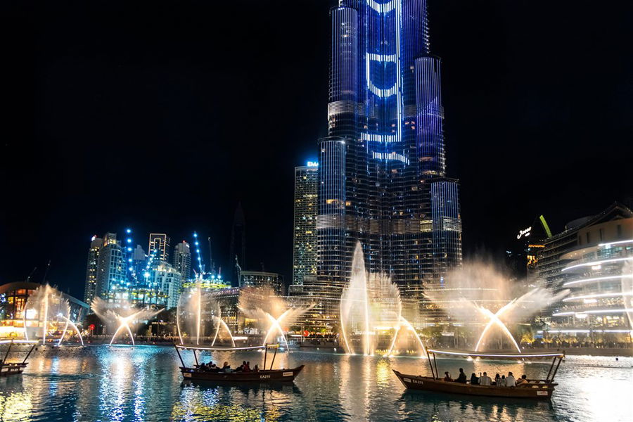 The Dubai Fountain display illuminated at night with tour boats in front of choreographed fountains in the Burj Khalifa Lake